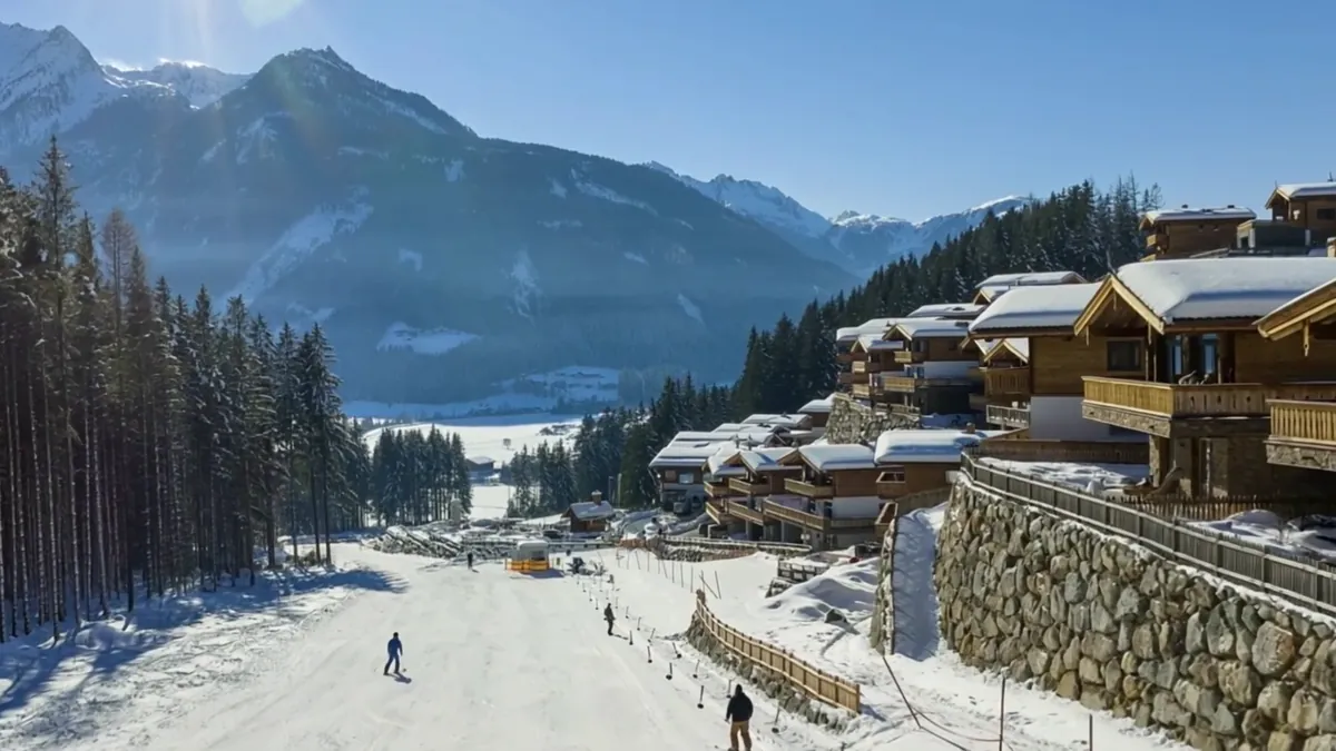 Die Piste am Chaletdorf im Winter mit Skifahrern, daneben die Chalets am Hang