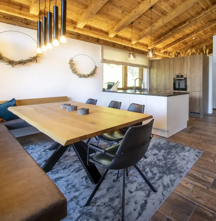 Esstisch aus Holz mit Eckbank und Stühlen, dahinter die Küche
