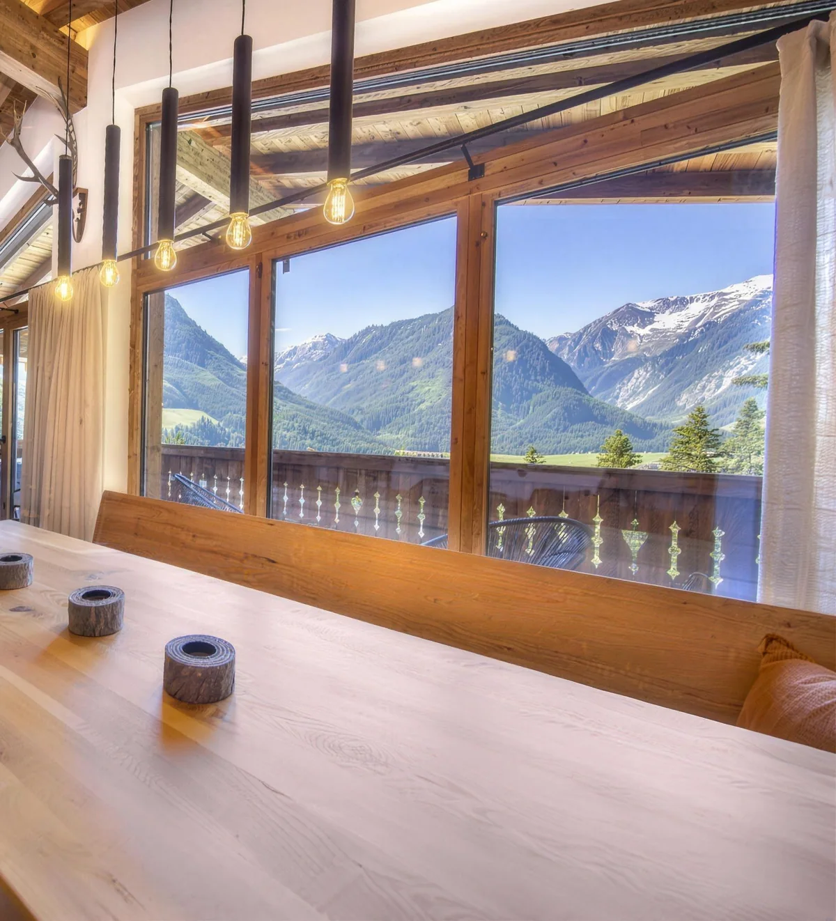 Langer Holztisch vor der Fensterfront, dahinter das Tal und die Berge