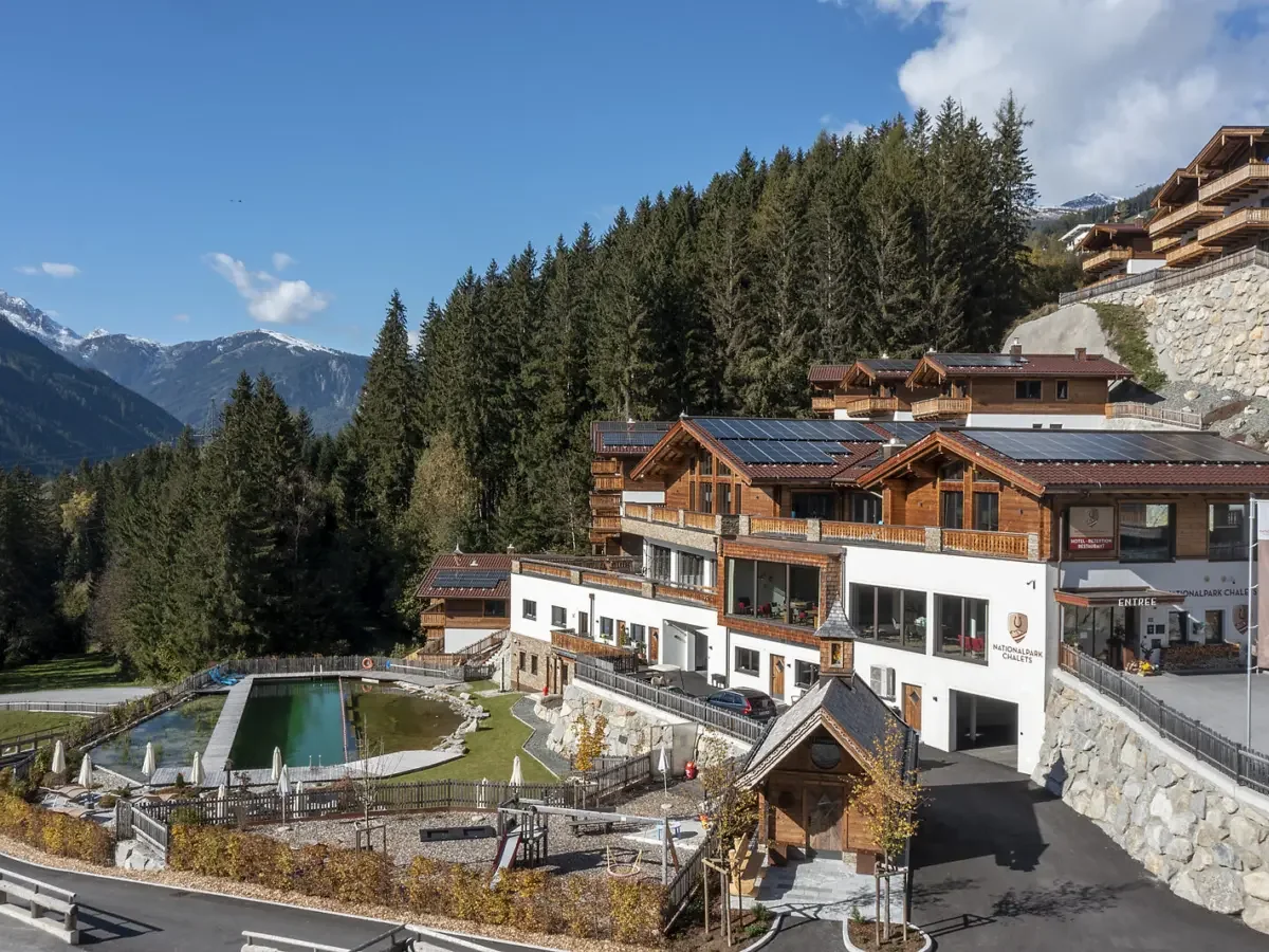 Das Chaletdorf im Sommer mit dem Naturpool, dahinter der Wald und die Berge