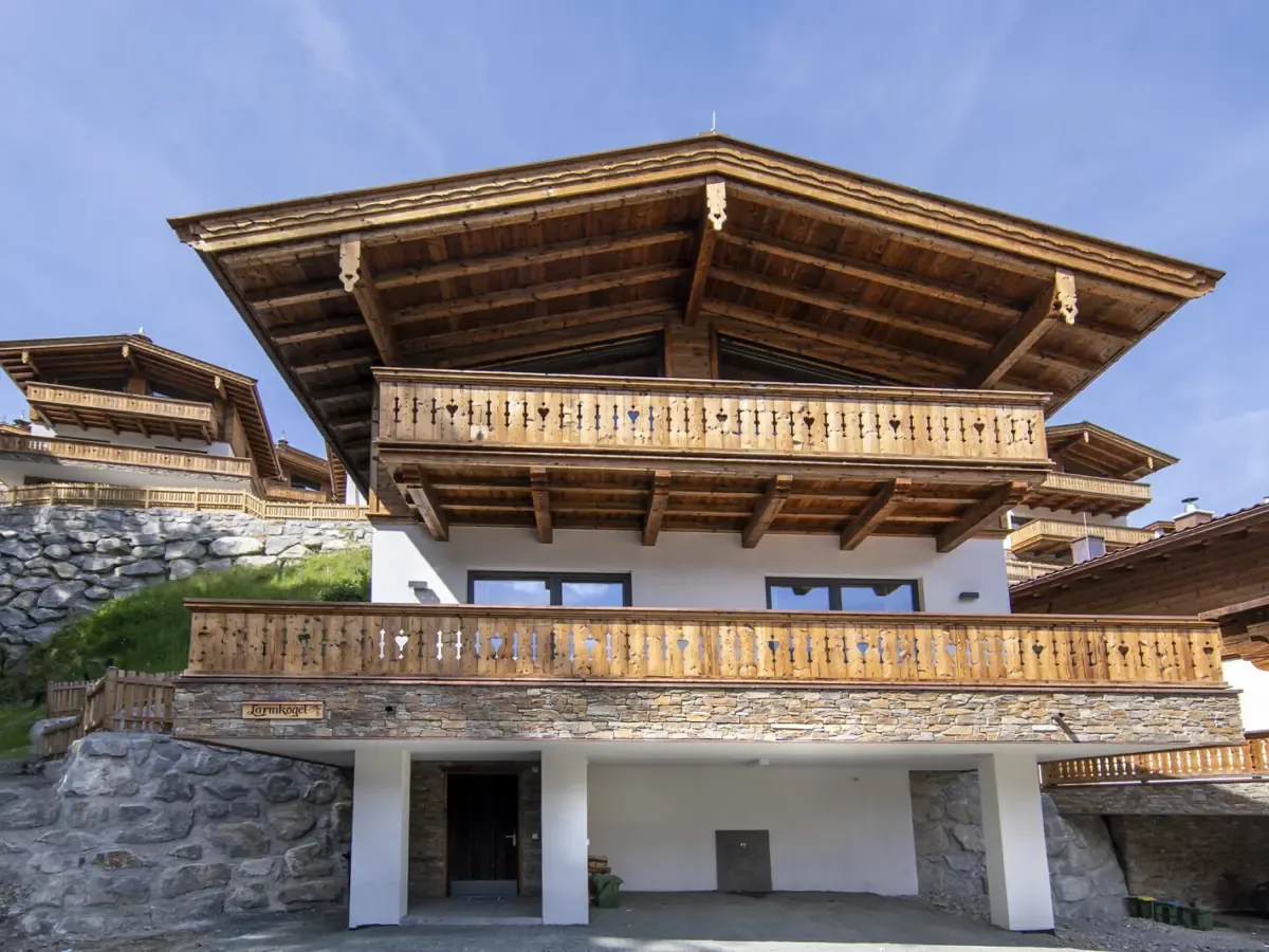 Das Chalet von außen im Sommer, Holzbalkone über einem Sockel aus Naturstein, daneben die Nachbarchalets