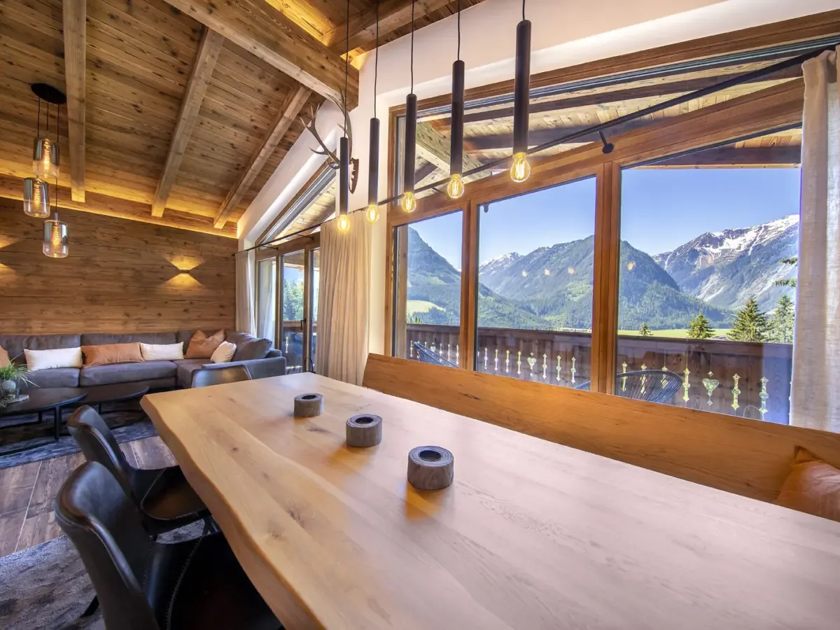 Der lange Esstisch am Fenster, dahinter das Sofa und der Blick über das Tal auf die Berge