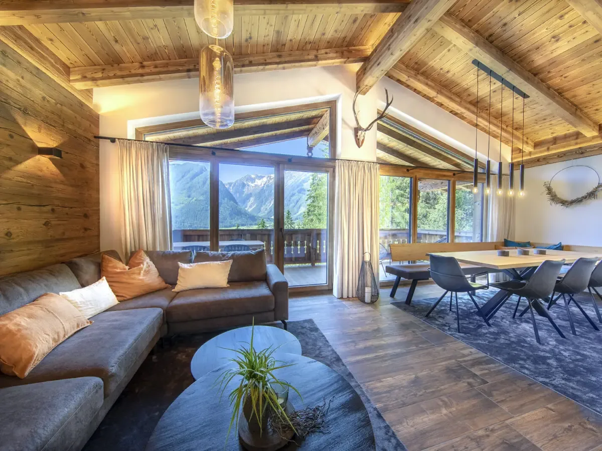 Der Wohnraum auf der obersten Etage unter dem offenen Holzdach, Sofa, Esstisch und das Panoramafenster über das Tal