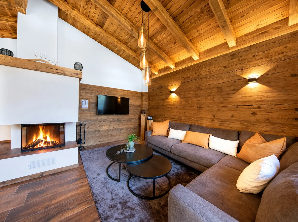 Der Kamin mit Glasscheibe und brennendem Feuer, daneben das Sofa vor der Altholzwand