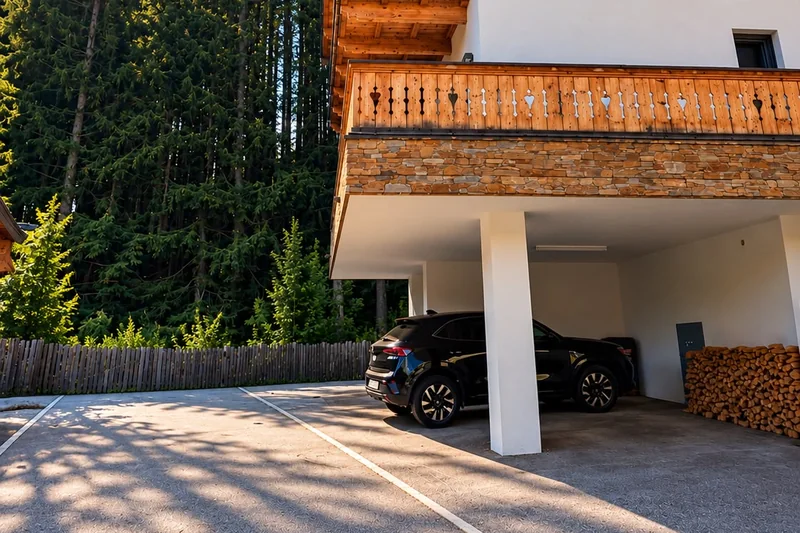 Das Chalet von der Seite mit dem überdachten Stellplatz, daneben gestapeltes Kaminholz und der Wald