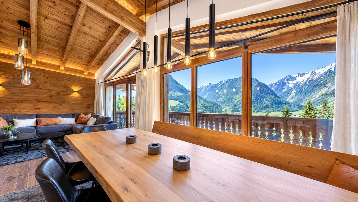 Der lange Holztisch am Panoramafenster, dahinter das Tal und die Berge